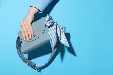 Photo of Woman showing stylish handbag on light blue background, closeup. Space for text