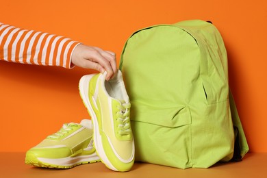 Photo of Woman with stylish neon lime sneakers and backpack on color background, closeup