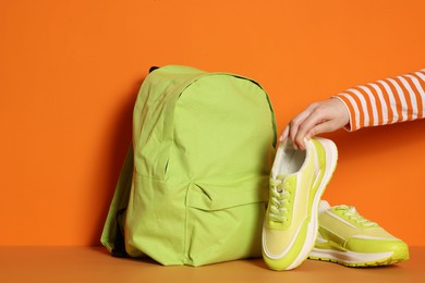 Photo of Woman with stylish neon lime sneakers and backpack on color background, closeup