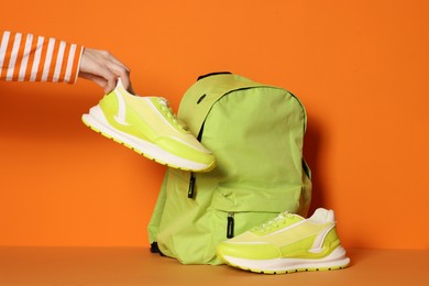 Photo of Woman with stylish neon lime sneakers and backpack on color background, closeup