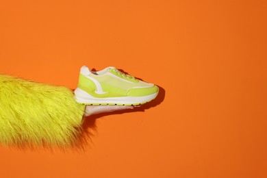 Photo of Woman showing stylish neon lime sneaker on orange background, closeup. Space for text