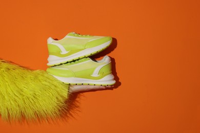 Photo of Woman showing stylish neon lime sneakers on orange background, closeup. Space for text