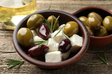 Photo of Marinated olives with feta cheese, oil and rosemary on wooden table, closeup