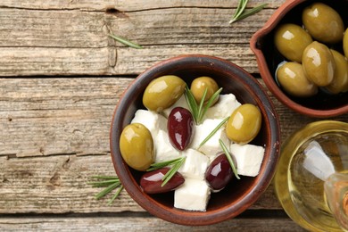 Photo of Marinated olives with feta cheese, oil and rosemary on wooden table, top view. Space for text