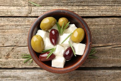 Photo of Marinated olives with feta cheese and rosemary on wooden table, top view