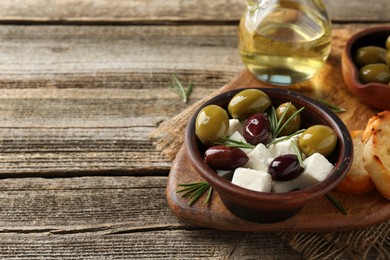 Photo of Marinated olives with feta cheese, oil and rosemary on wooden table, closeup. Space for text