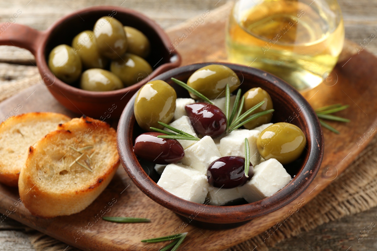 Photo of Marinated olives with feta cheese, bread pieces, oil and rosemary on wooden table, closeup