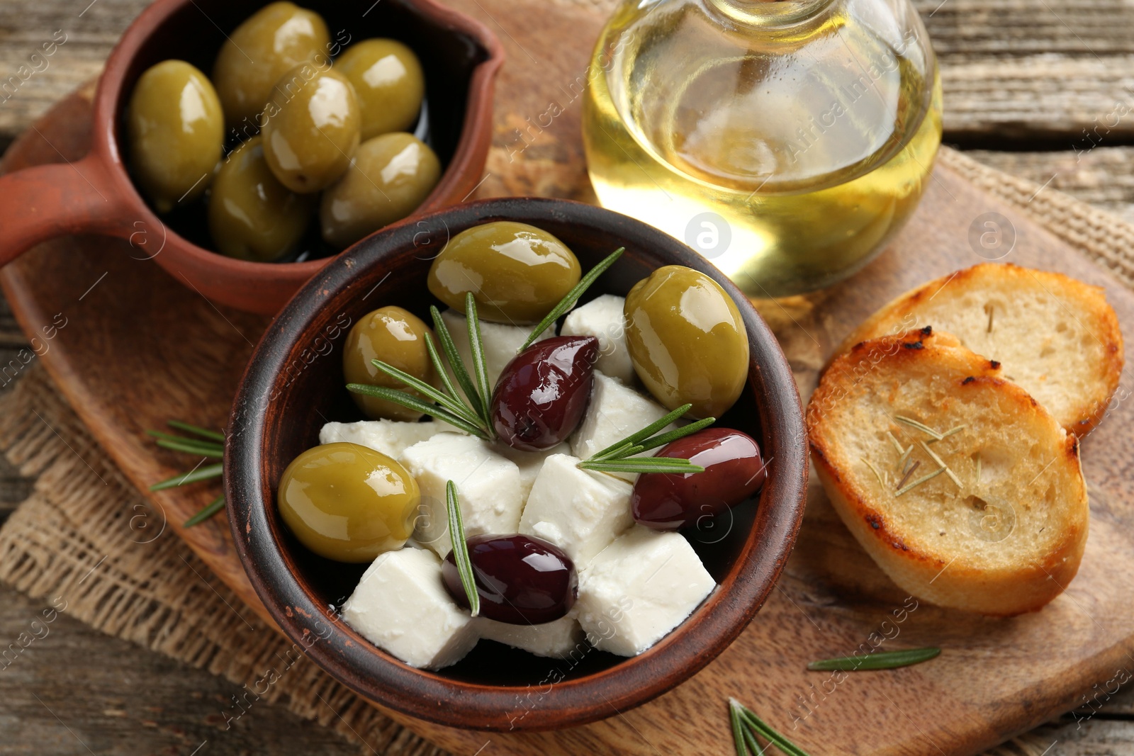 Photo of Marinated olives with feta cheese, bread pieces, oil and rosemary on wooden table, closeup