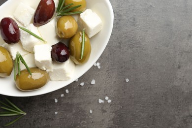 Photo of Marinated olives with feta cheese, salt and rosemary on grey table, top view. Space for text