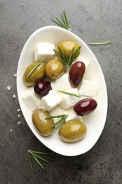 Photo of Marinated olives with feta cheese, salt and rosemary on grey table, top view