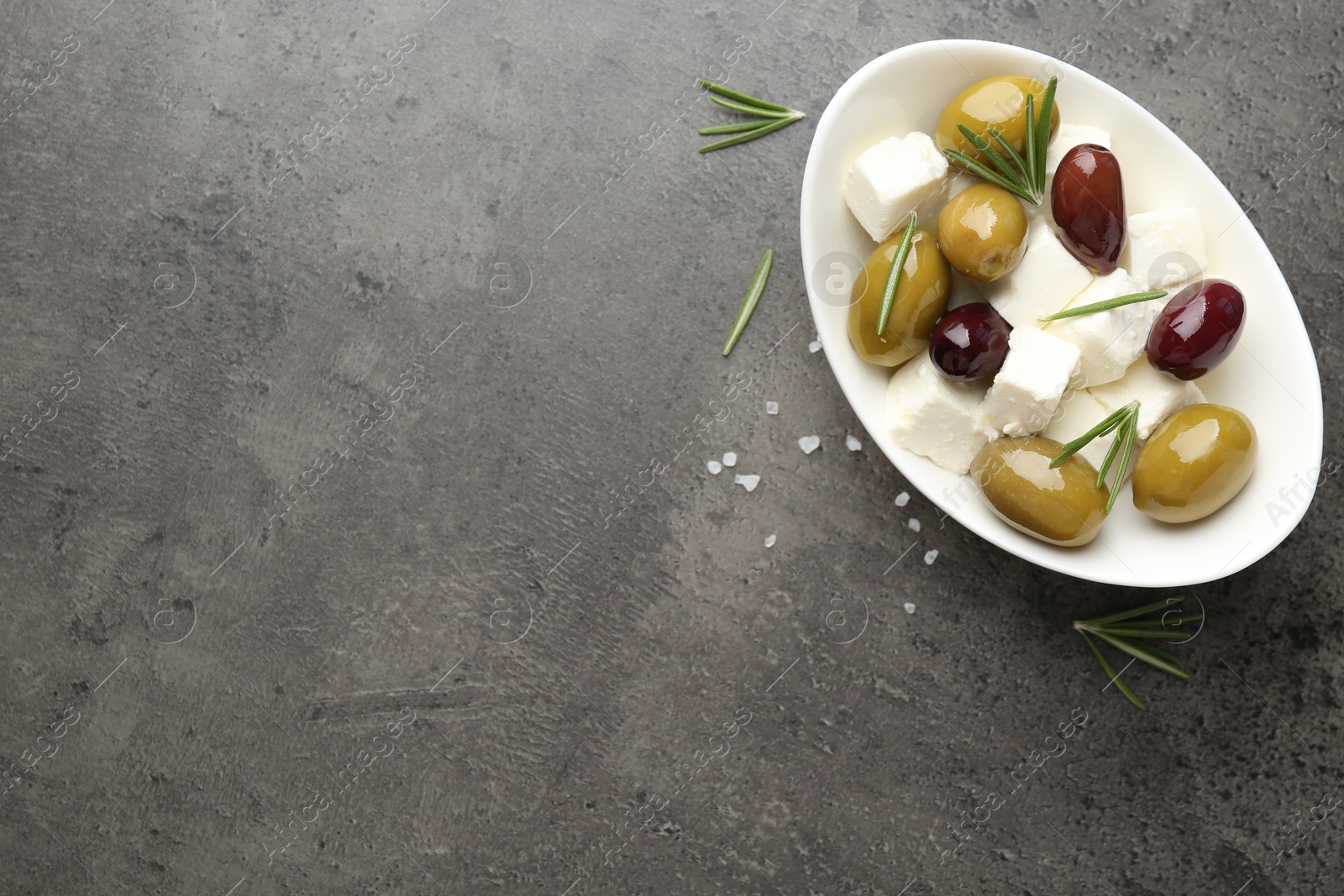 Photo of Marinated olives with feta cheese, salt and rosemary on grey table, top view. Space for text