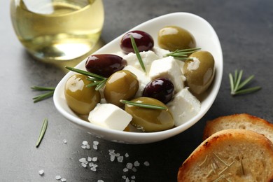 Photo of Marinated olives with feta cheese, bread pieces, oil, salt and rosemary on grey table, closeup