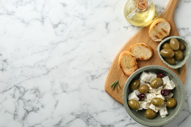 Photo of Marinated olives with feta cheese, bread pieces, oil and rosemary on white marble table, flat lay. Space for text