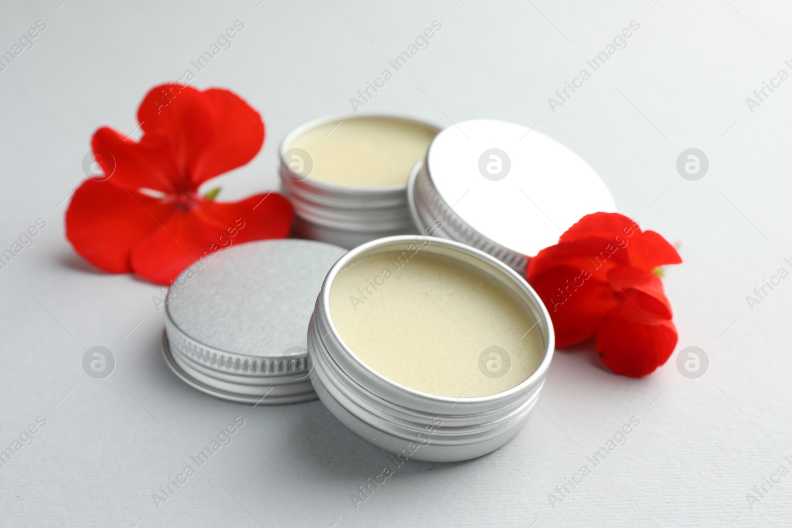 Photo of Lip balms and red flowers on white background, closeup