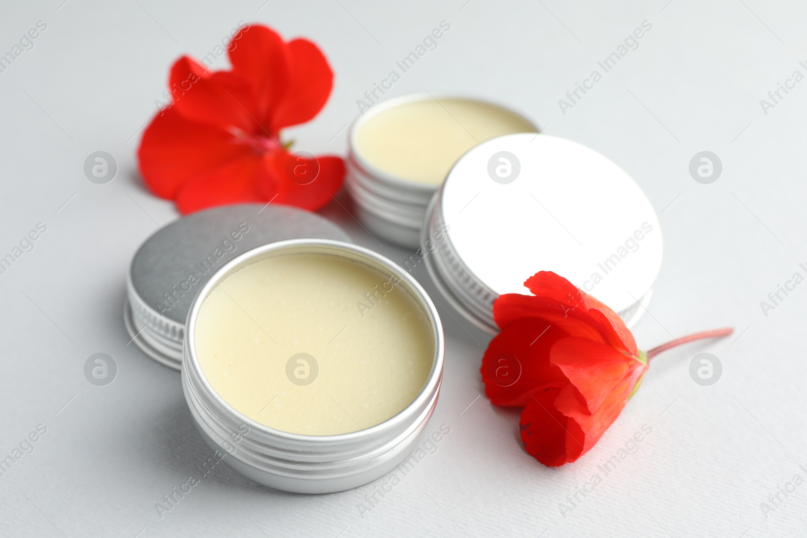 Photo of Lip balms and red flowers on white background, closeup