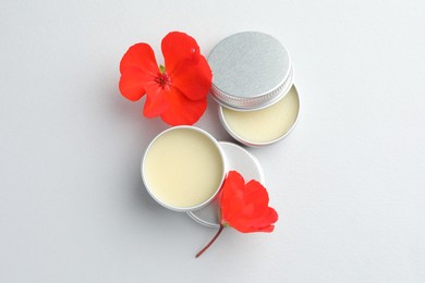 Photo of Lip balms and red flowers on white background, top view