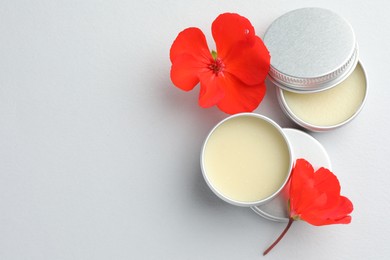 Photo of Lip balms and red flowers on white background, top view. Space for text