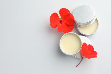 Photo of Lip balms and red flowers on white background, top view. Space for text