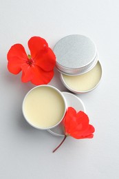 Photo of Lip balms and red flowers on white background, top view