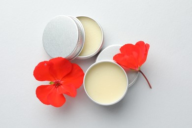 Photo of Lip balms and red flowers on white background, top view