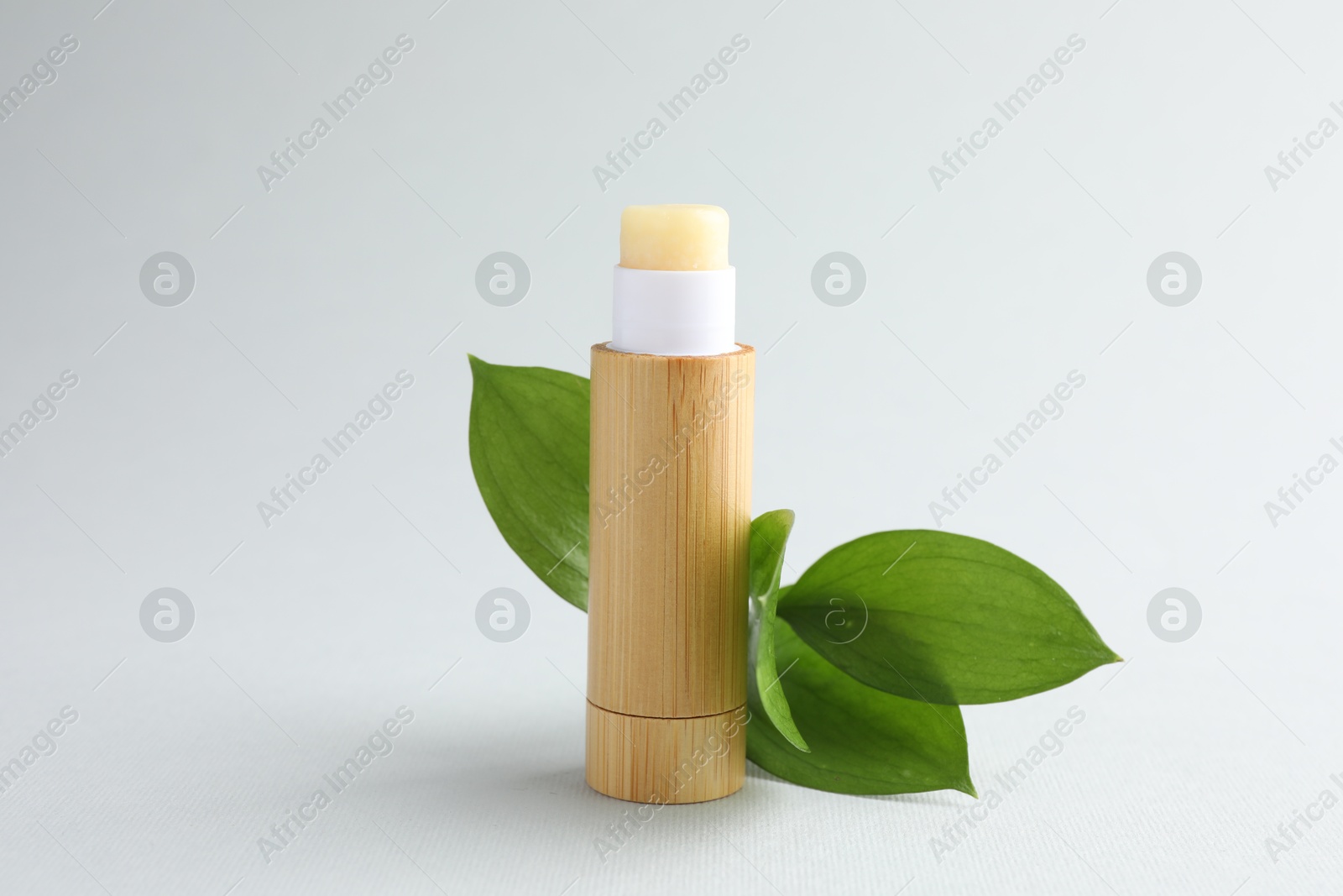 Photo of Lip balm and leaves on white background, closeup