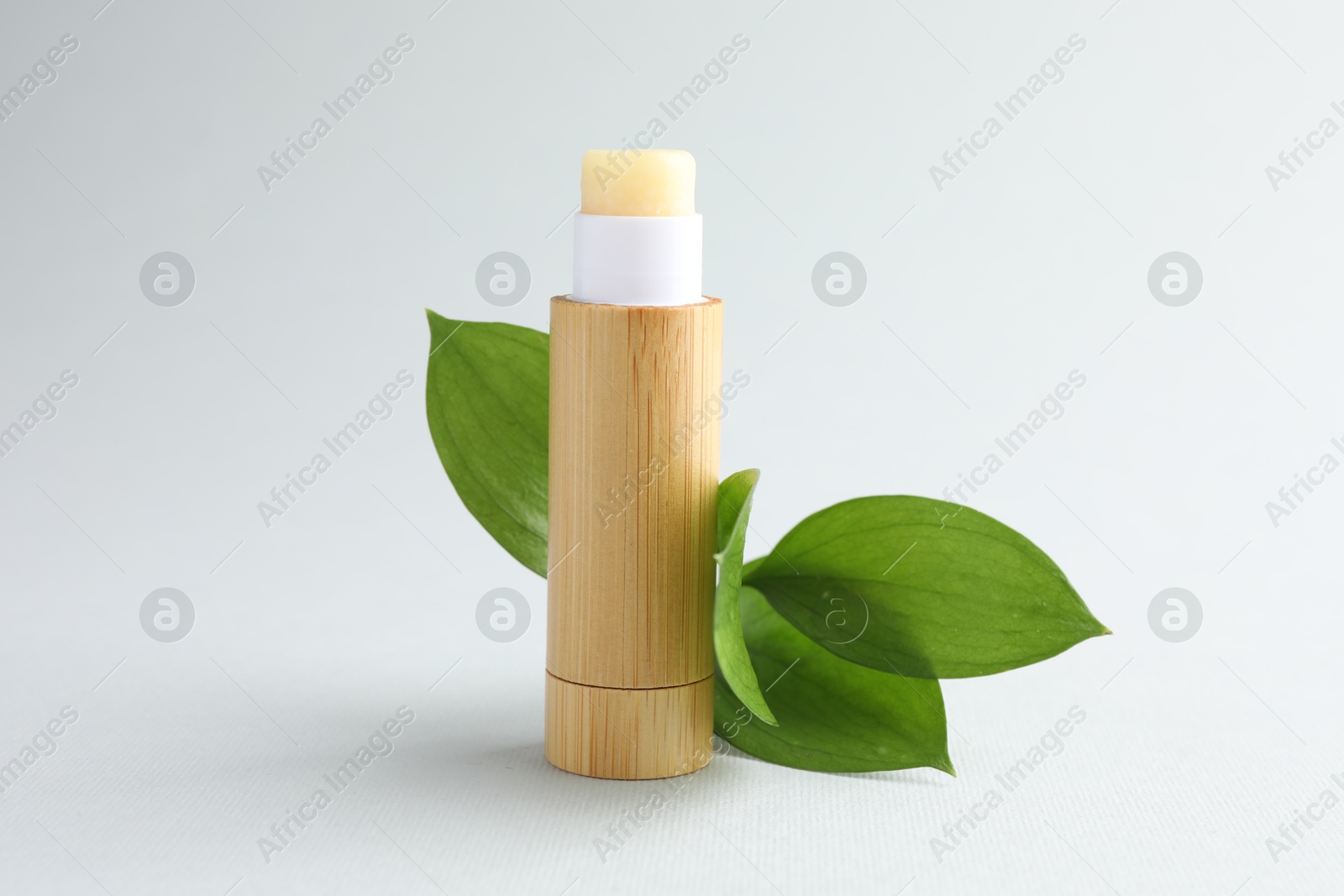 Photo of Lip balm and leaves on white background, closeup