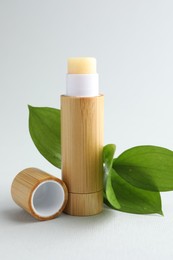 Photo of Lip balm and leaves on white background, closeup