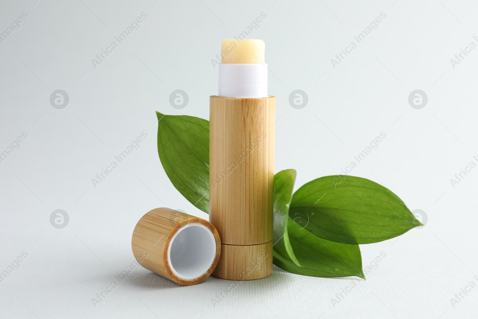 Photo of Lip balm and leaves on white background, closeup