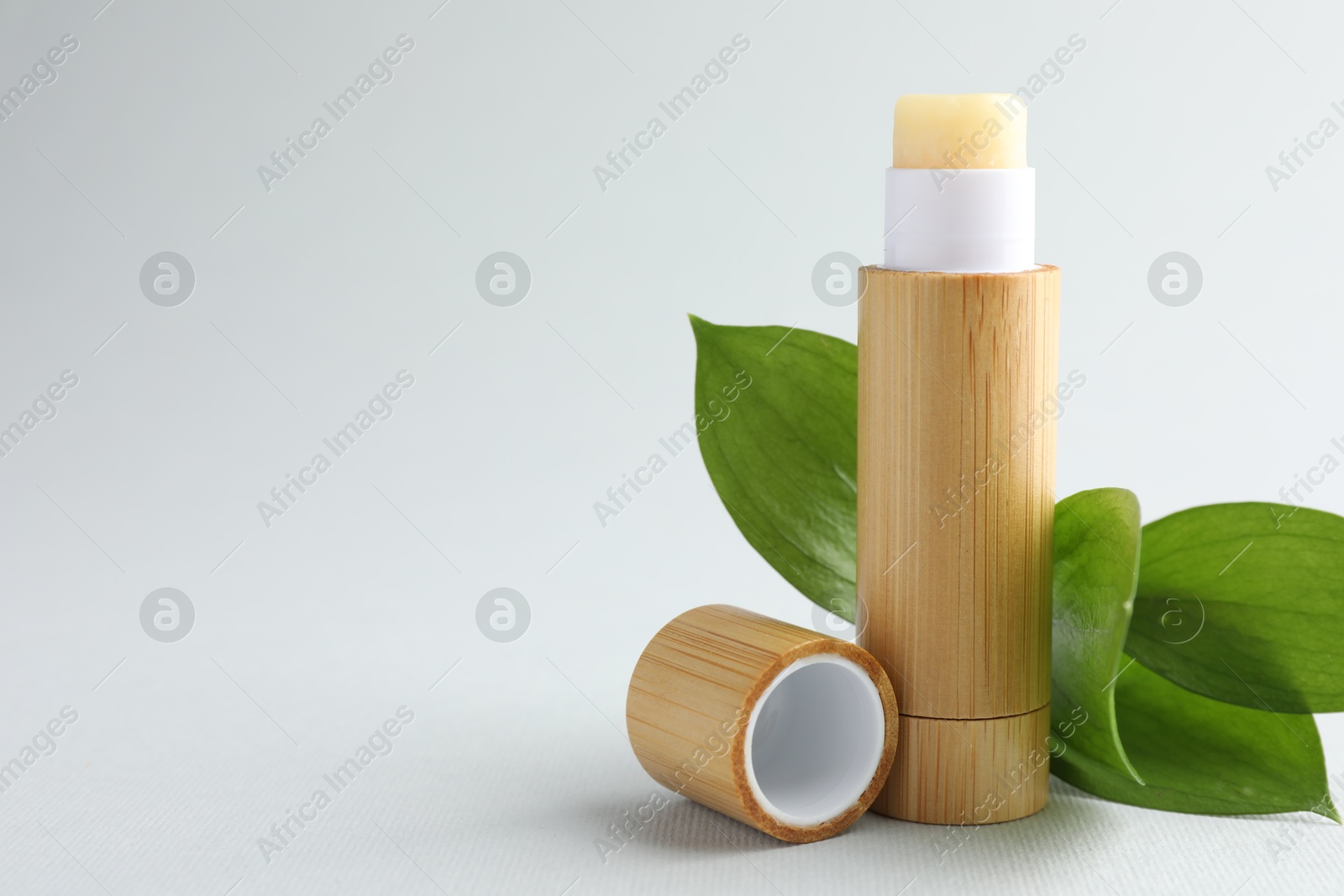 Photo of Lip balm and leaves on white background, closeup. Space for text