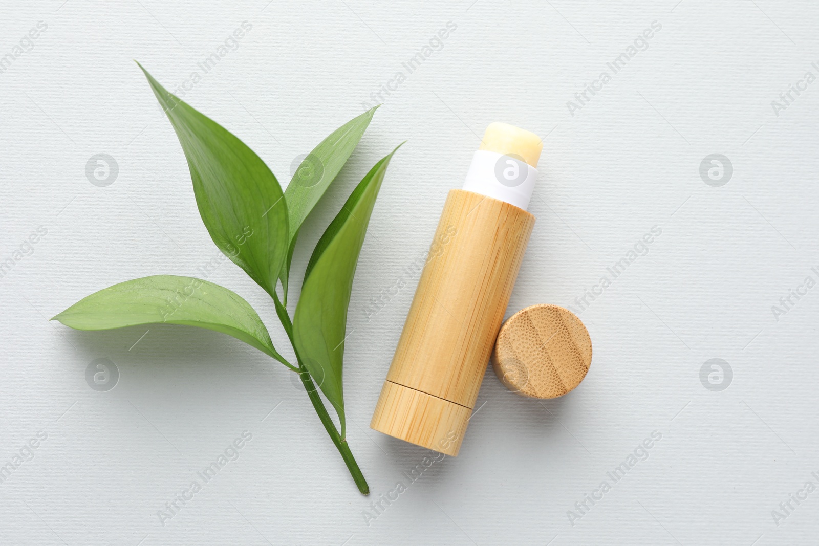 Photo of Lip balm and leaves on white background, top view