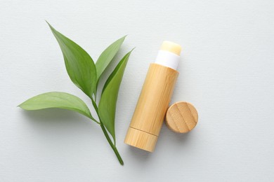 Photo of Lip balm and leaves on white background, top view