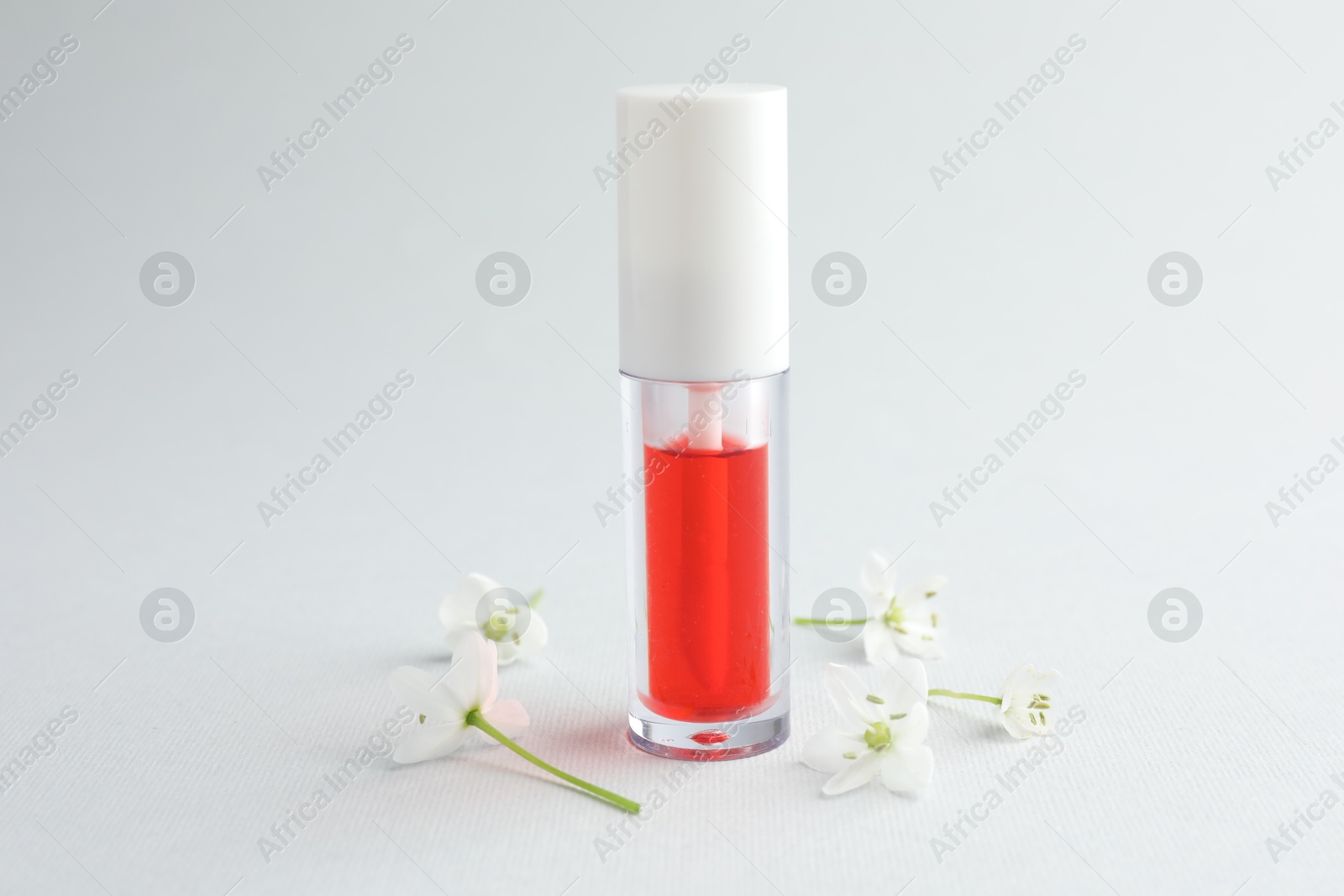 Photo of Lip oil and flowers on white background, closeup