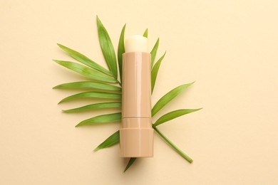 Photo of Lip balm and leaves on beige background, top view