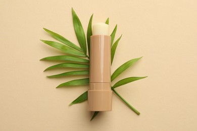 Photo of Lip balm and leaves on beige background, top view