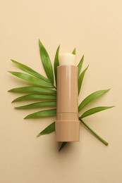 Photo of Lip balm and leaves on beige background, top view