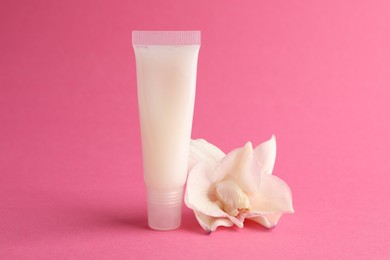 Photo of Lip balm and flower on pink background, closeup