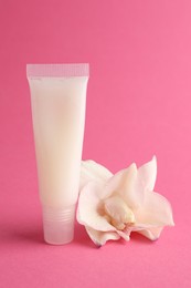 Photo of Lip balm and flower on pink background, closeup