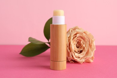 Photo of Lip balm and flower on pink background, closeup