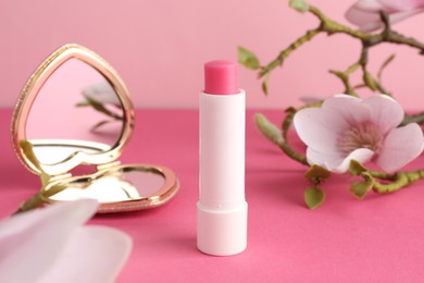 Photo of Lip balm, heart shaped mirror and flowers on pink background, closeup