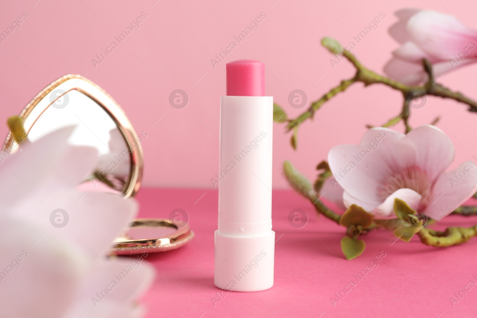 Photo of Lip balm, heart shaped mirror and flowers on pink background, closeup