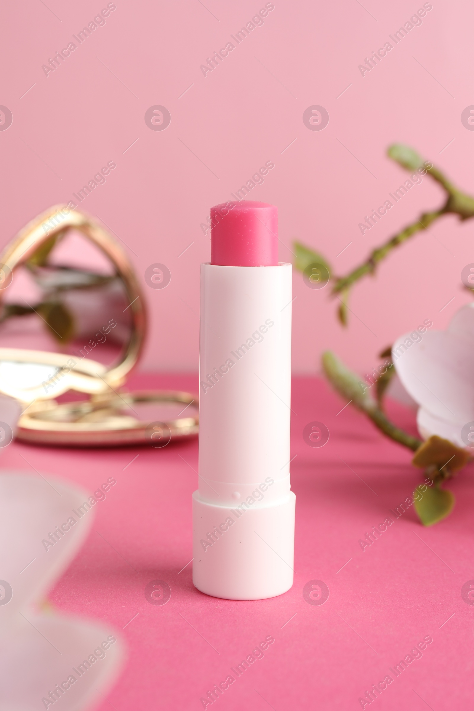 Photo of Lip balm, heart shaped mirror and flowers on pink background, closeup