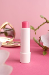 Photo of Lip balm, heart shaped mirror and flowers on pink background, closeup