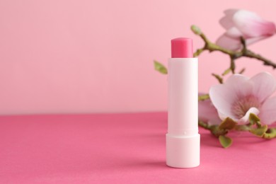 Photo of Lip balm and flowers on pink background, closeup. Space for text