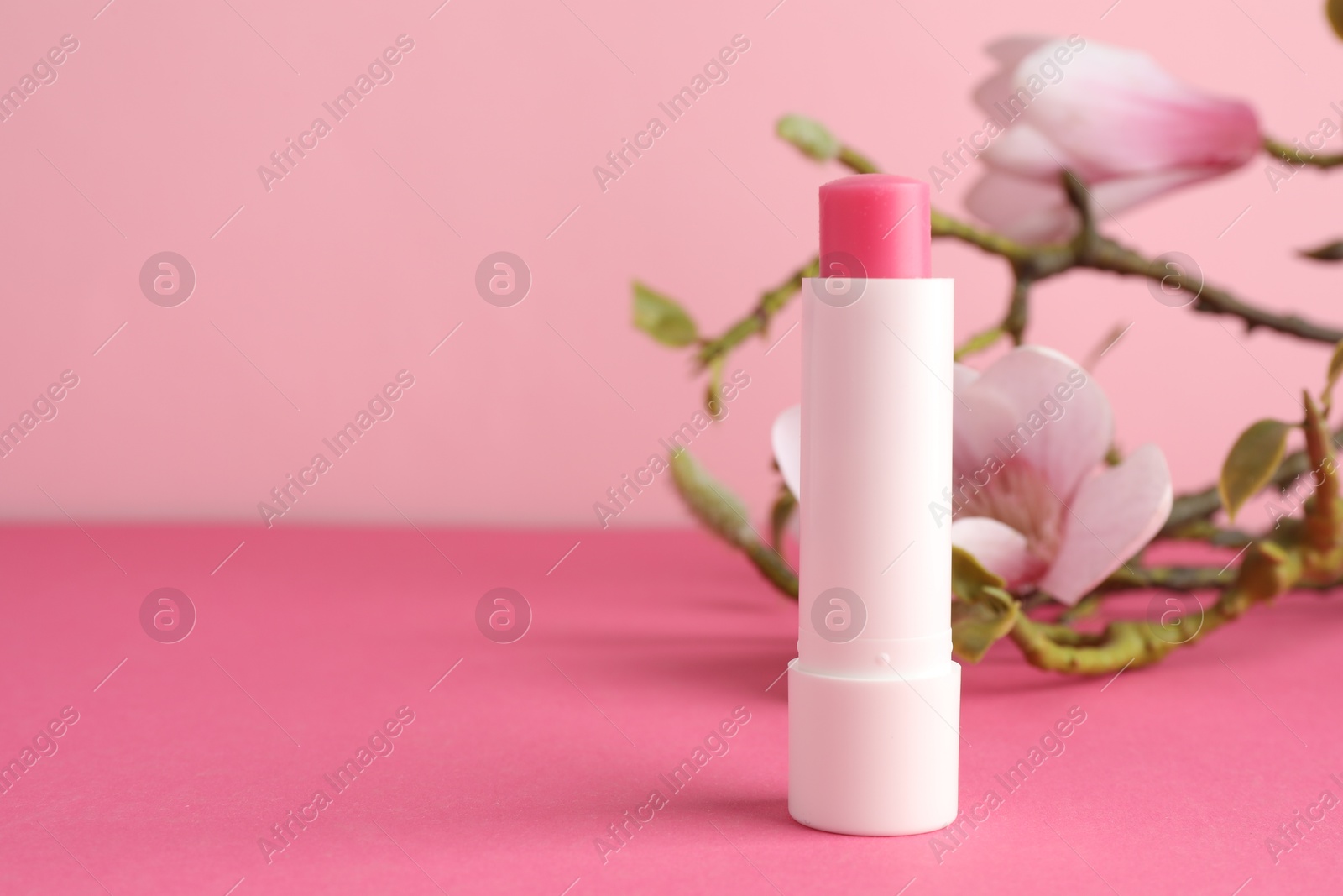 Photo of Lip balm and flowers on pink background, closeup. Space for text