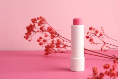 Photo of Lip balm and flowers on pink background, closeup. Space for text