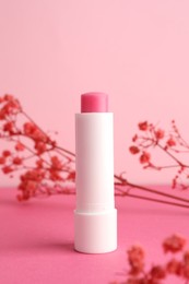 Photo of Lip balm and flowers on pink background, closeup