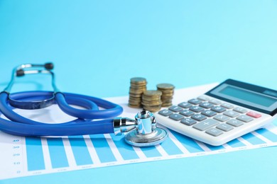 Photo of Stethoscope, chart, calculator and coins on light blue background, closeup