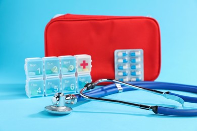 Photo of Stethoscope, first aid kit and pills on light blue background, closeup