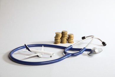 Photo of Stethoscope airplane model and coins on light background