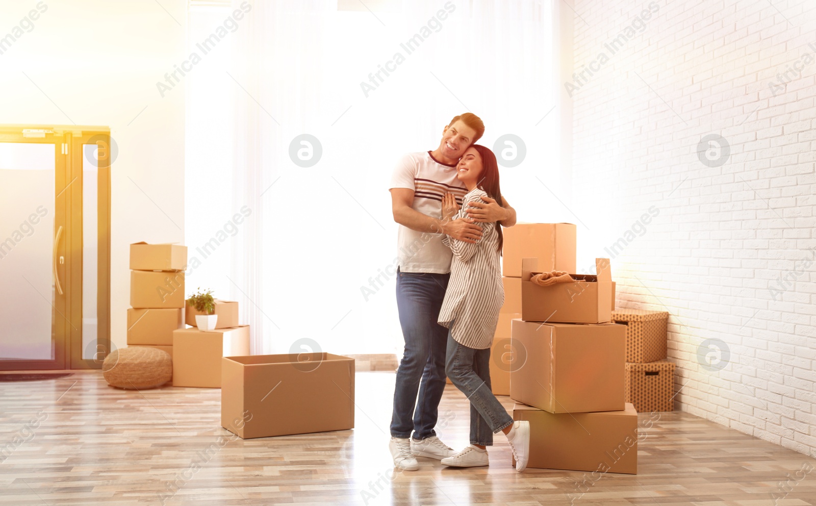 Image of Happy couple in sunlit room with cardboard boxes on moving day